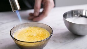 Pek karamelizira sladkor na vrhu crème brûléeja s kuhinjskim gorilnikom.